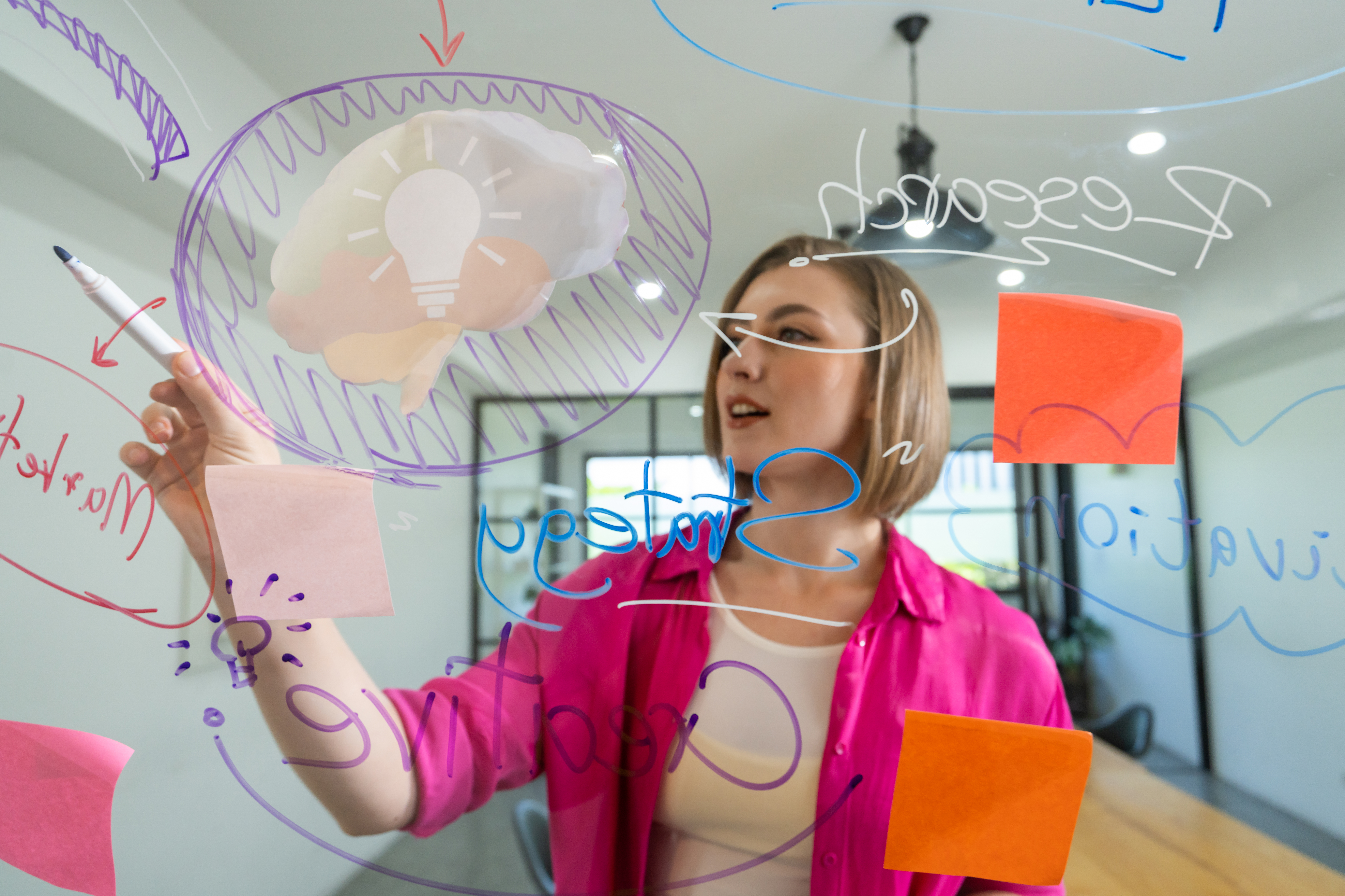 Mulher criando estratégias em um painel transparente durante uma sessão de brainstorming, representando o processo de design iterativo