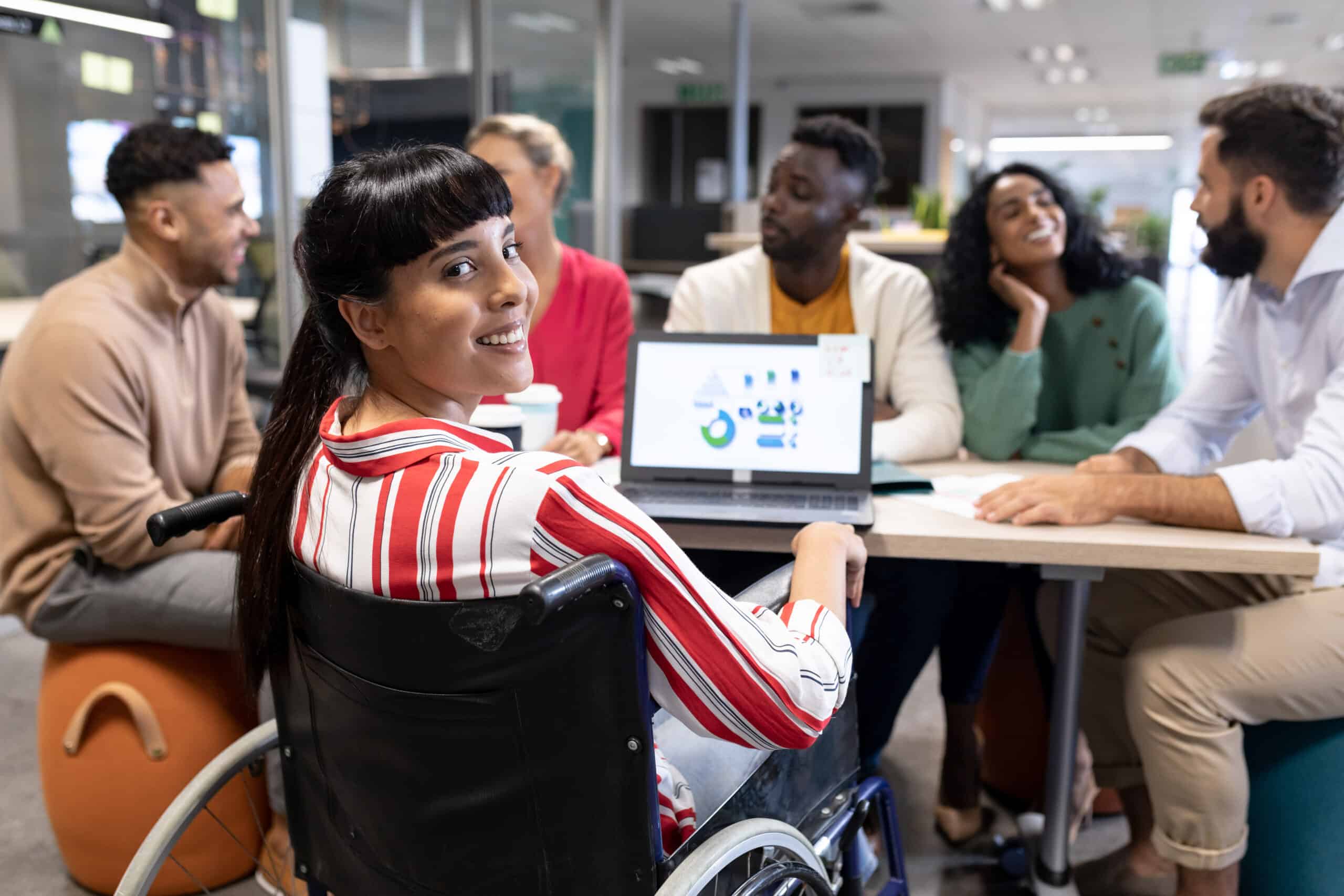 Mulher em cadeira de rodas participa de reunião sobre design acessível, inclusivo e universal com equipe diversa em ambiente corporativo.